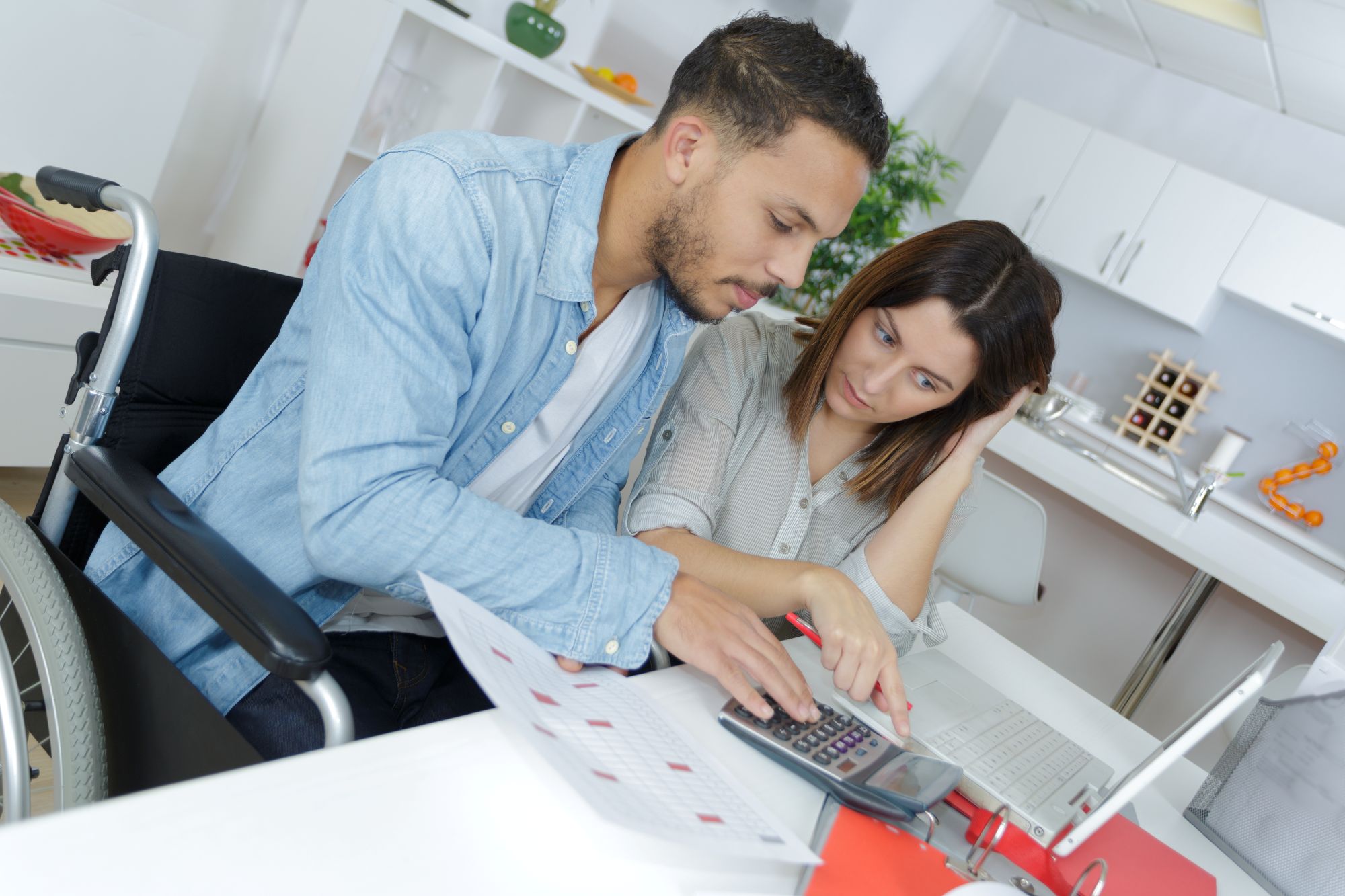 Young man in a wheelchair reviewing budget at a desk with young woman